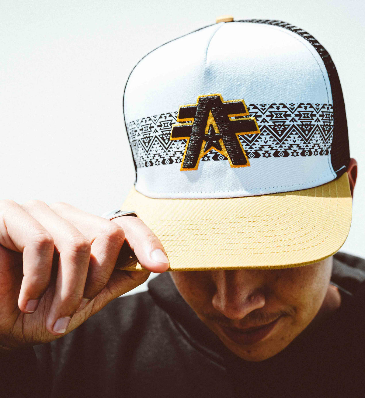 Person wearing a white and beige cap with a logo, against a neutral background