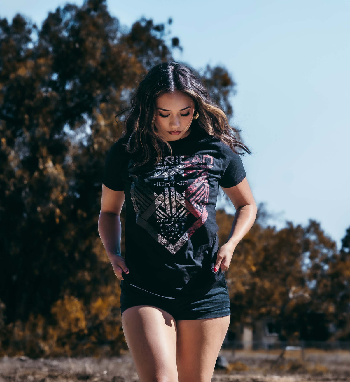 Woman wearing a black graphic t-shirt and shorts outdoors with trees in the background
