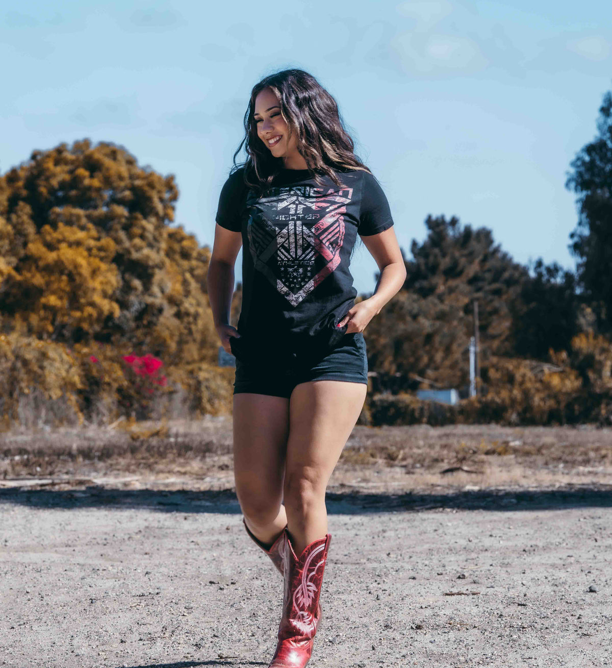 Woman wearing a black t-shirt with a graphic design and red cowboy boots in an outdoor setting.