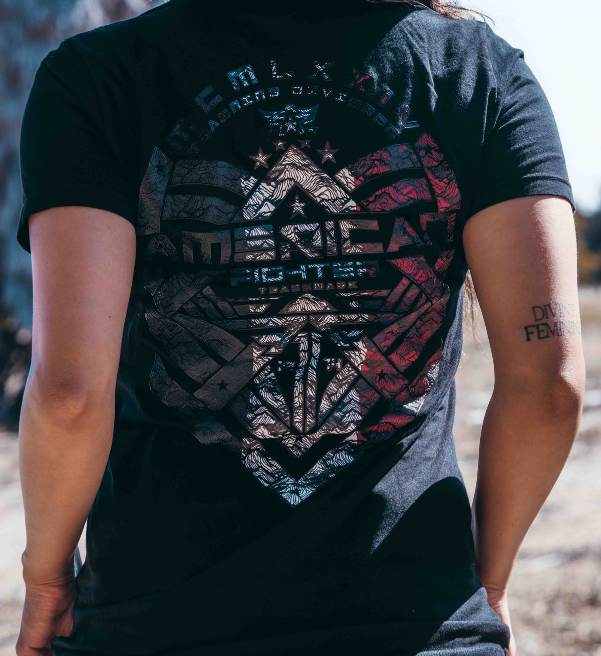Person wearing a black t-shirt with a graphic design on the back, standing outdoors.