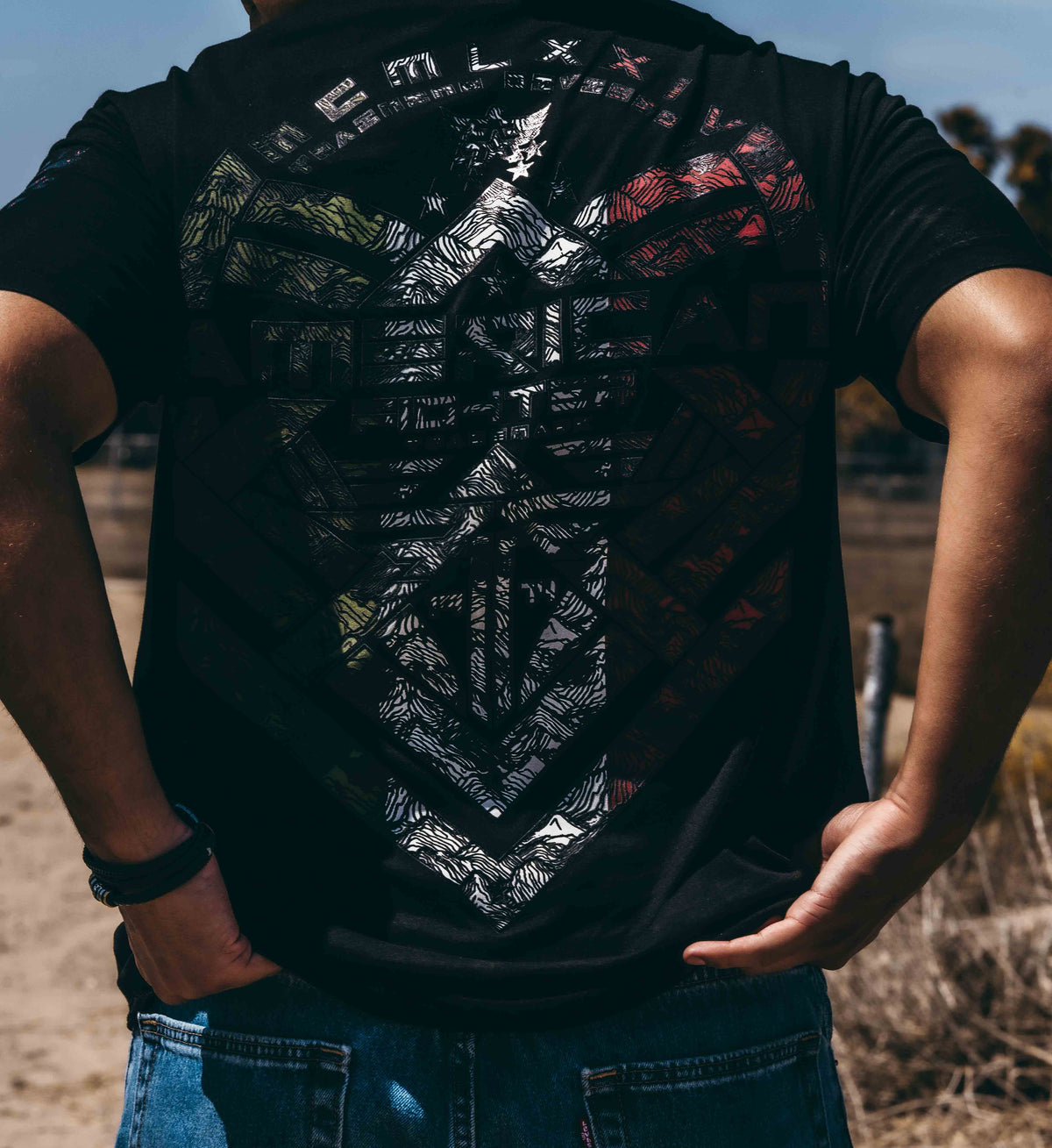 Person wearing a black t-shirt with a detailed design on the back, standing outdoors.
