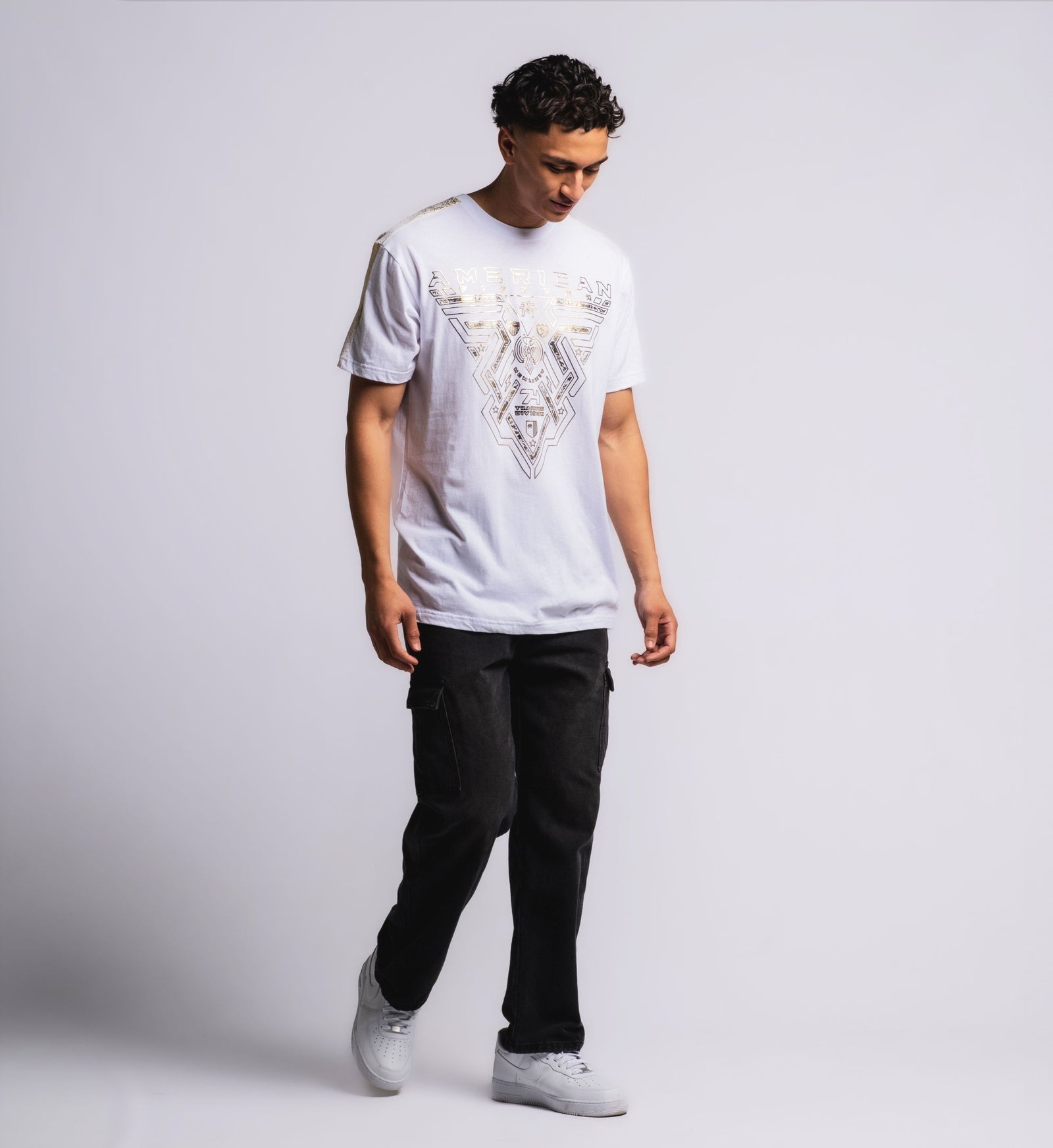 A male model wearing a white short-sleeved t-shirt with gold foil text and geometric patterns on the shoulder panels.