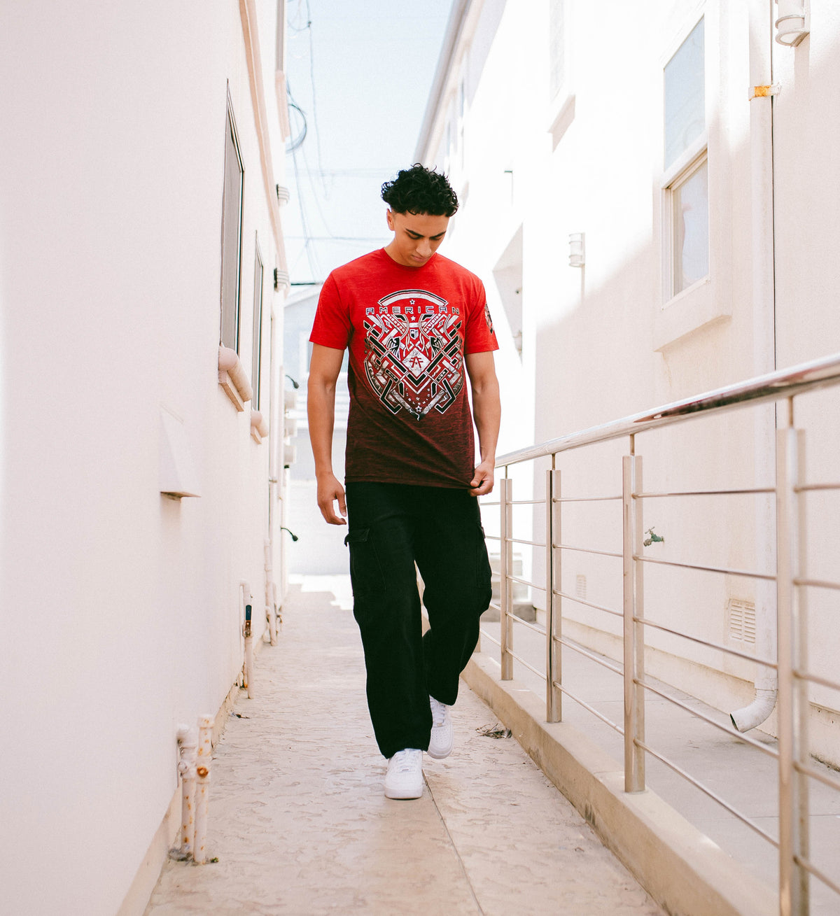 Man walking on a bridge wearing a red t-shirt with a graphic design.
