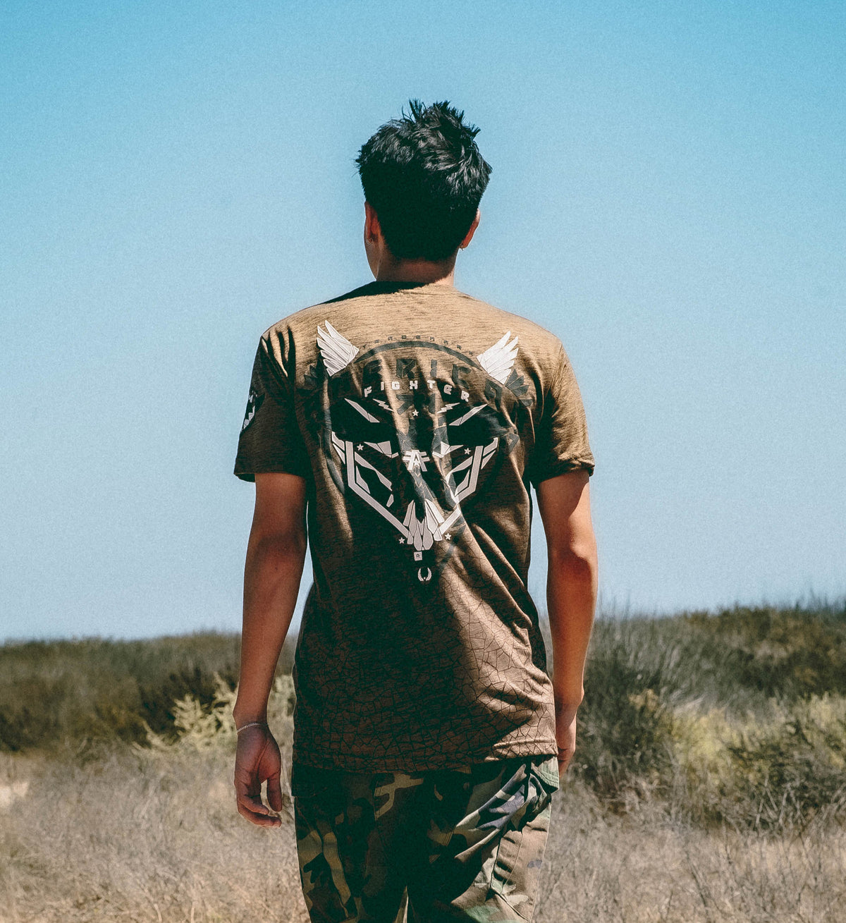 Person wearing a brown t-shirt with a graphic design walking in a desert landscape.