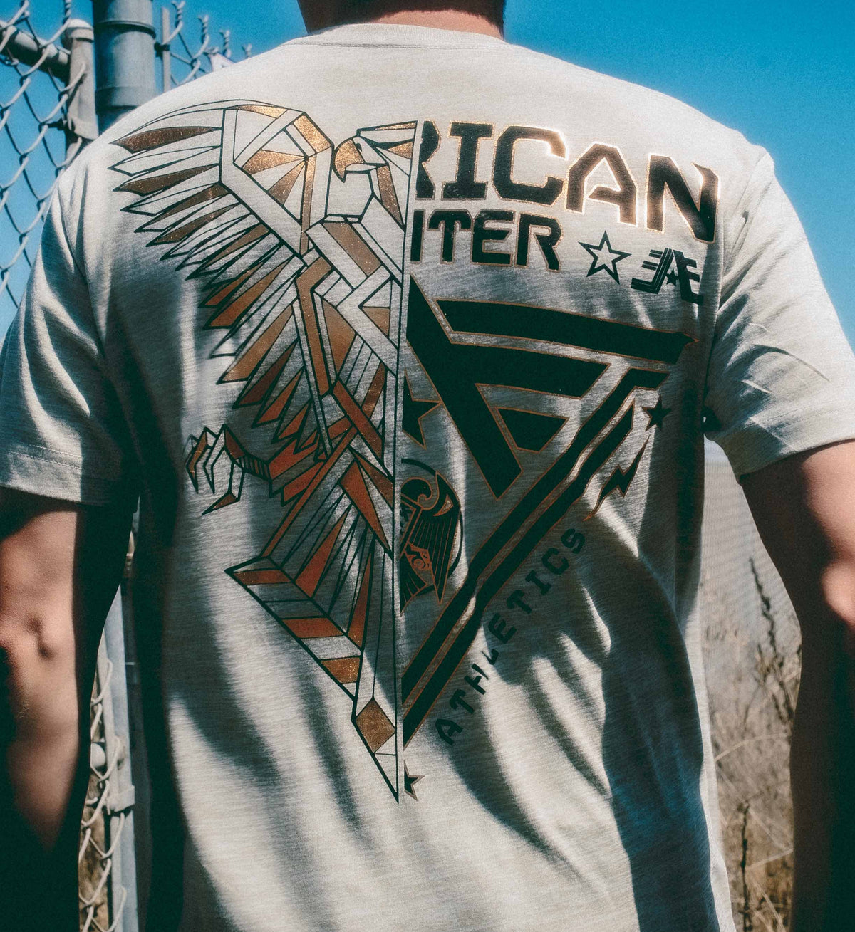 Person wearing a gray t-shirt with a graphic design on the back, standing outdoors.